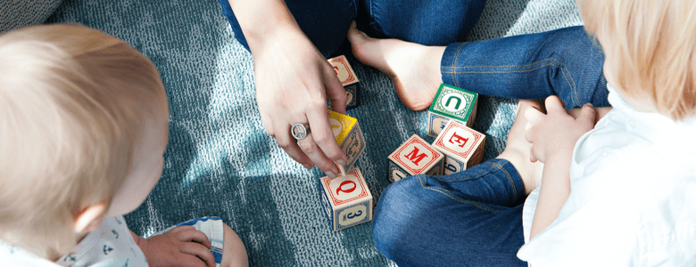 Two young children playing with wooden blocks with their mother