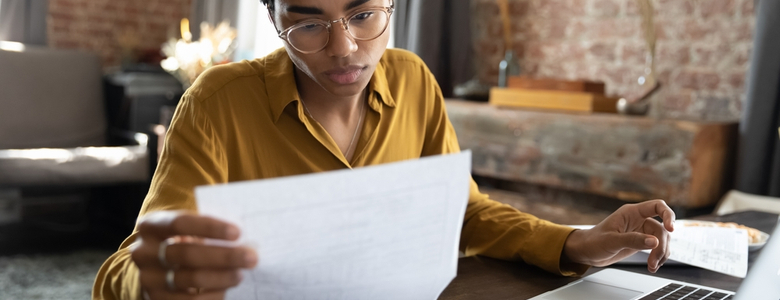 A woman looking through some paperwork with a laptop in front of her.