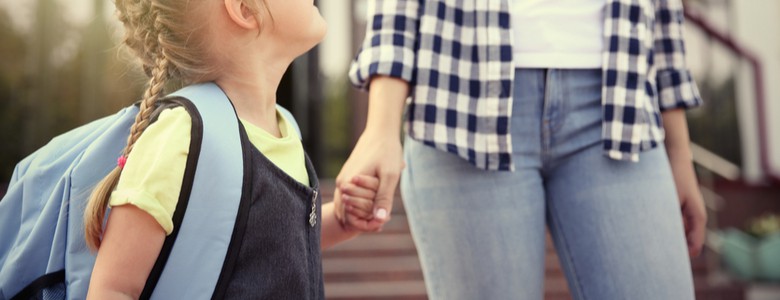 A mother and daughter holding hands as they walk to school.