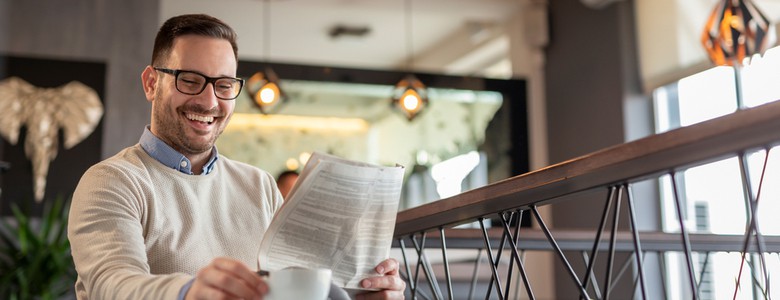 A man reading a newspaper while drinking coffee.