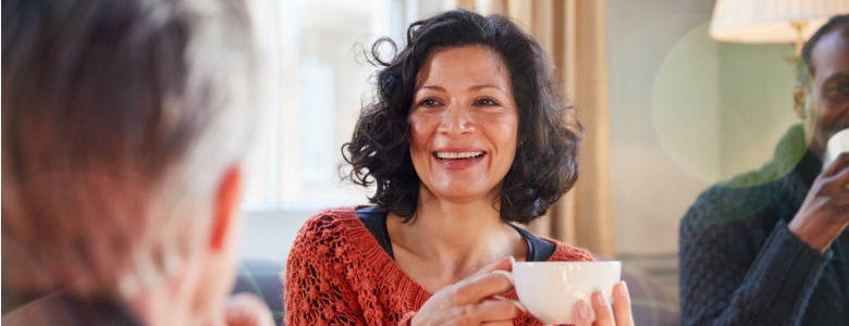 A woman talking to a man while drinking tea.