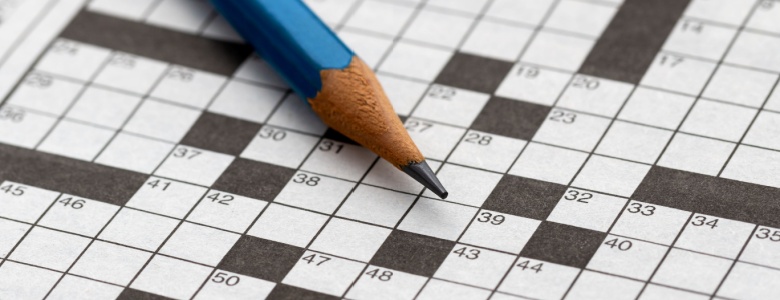 A close-up of an empty crossword puzzle with a pencil lying on top.