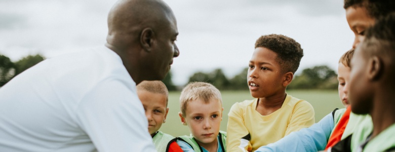A man coaching a junior football team.