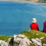 A family sitting on a clifftop overlooking a beach.