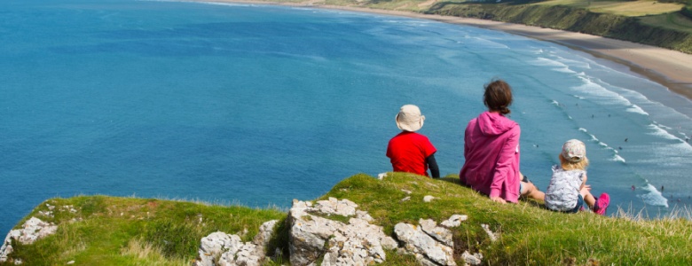 A family sitting on a clifftop overlooking a beach.