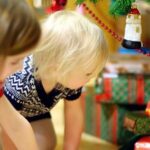 Two children looking at Christmas presents under a tree.