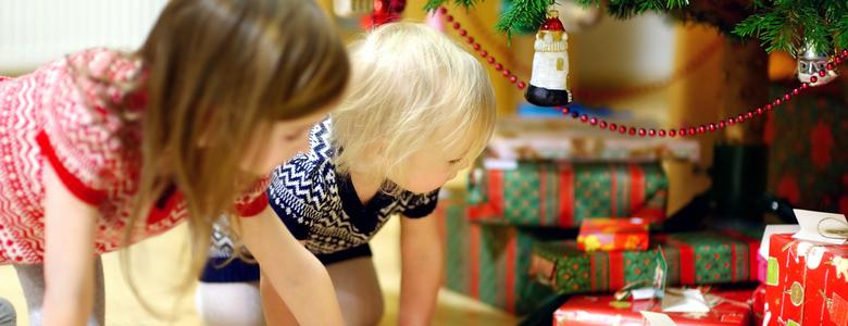 Two children looking at Christmas presents under a tree.