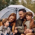 A young family sheltering under an umbrella and smiling