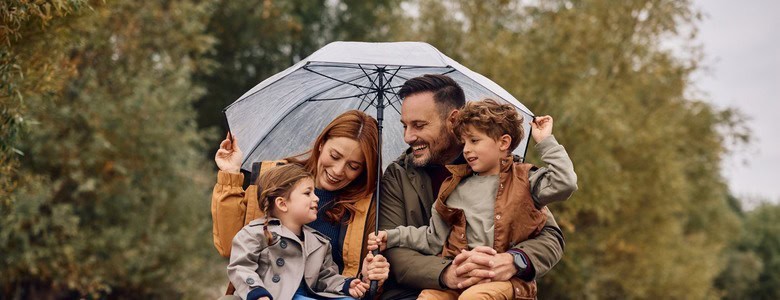 A young family sheltering under an umbrella and smiling