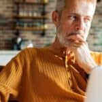 A man in his 50s thinking while using a laptop