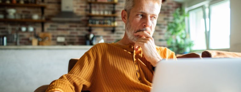 A man in his 50s thinking while using a laptop