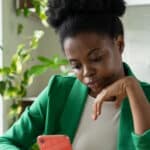 A woman procrastinating on her phone while sitting in front of a computer.