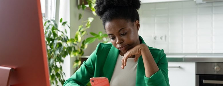 A woman procrastinating on her phone while sitting in front of a computer.