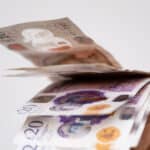A hand holding UK bank notes.