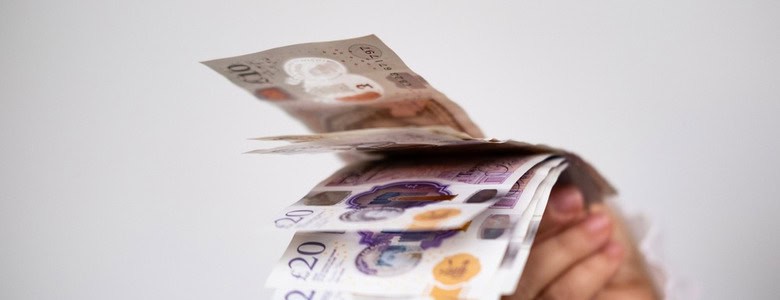 A hand holding UK bank notes.