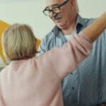 Two happy pensioners dancing at home, holding hands and having fun