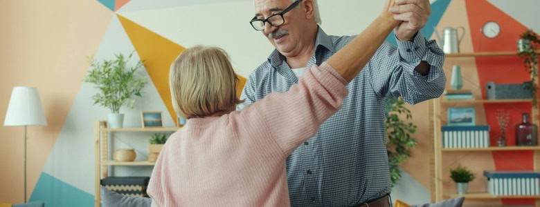 Two happy pensioners dancing at home, holding hands and having fun